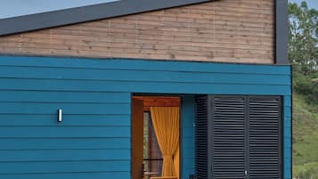 Una casa moderna con fachada azul, techo inclinado de madera y una puerta con contraventanas negras.
