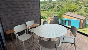 Ein Balkon mit rundem Tisch und vier Stühlen, der auf eine grüne Landschaft mit terrassenförmig angelegten Feldern blickt.