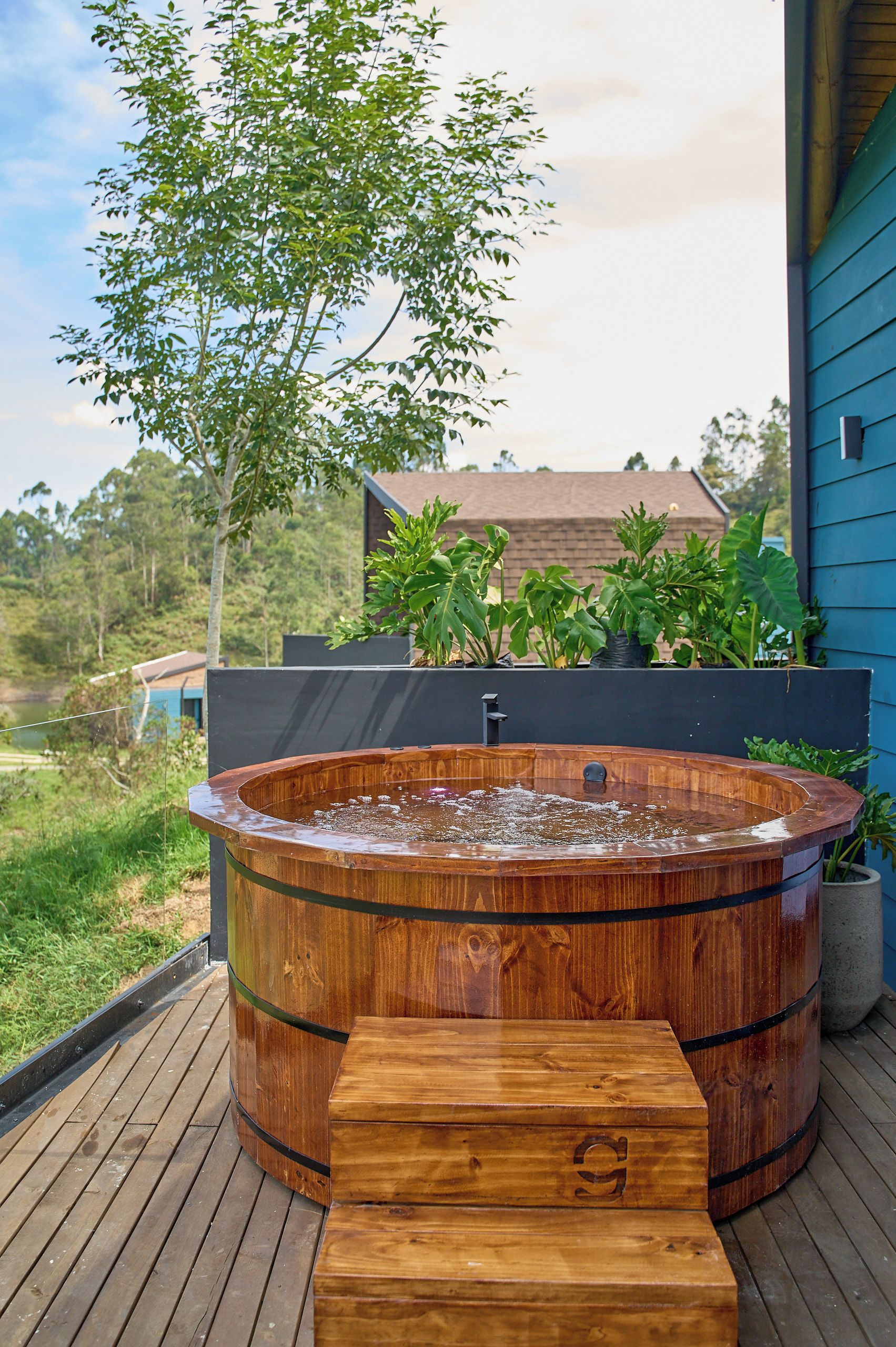 Un jacuzzi en una terraza de madera con vista a una casa y árboles al fondo.