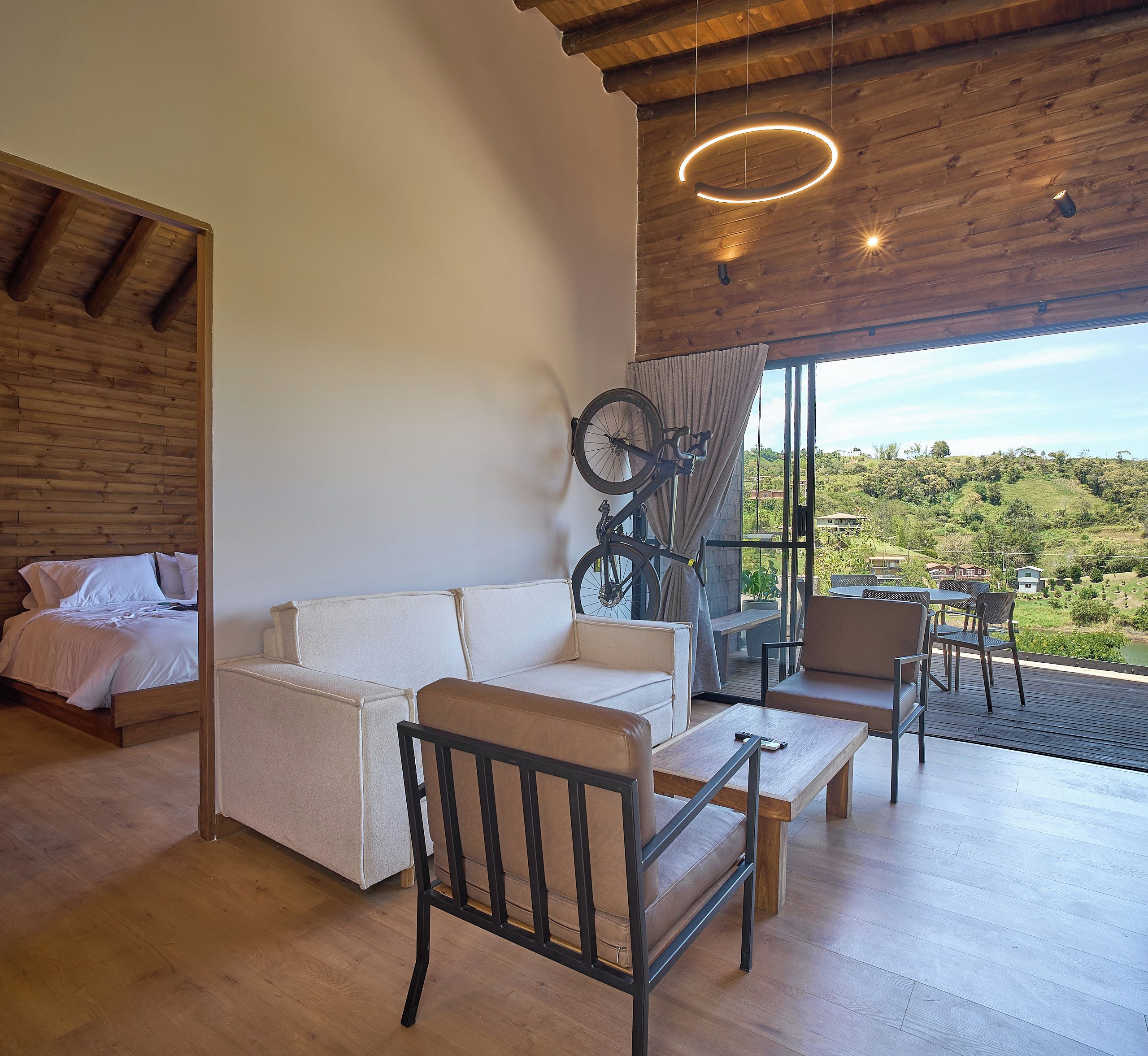 A modern room with a wooden ceiling, a sofa, a bicycle, and a view of a green landscape.