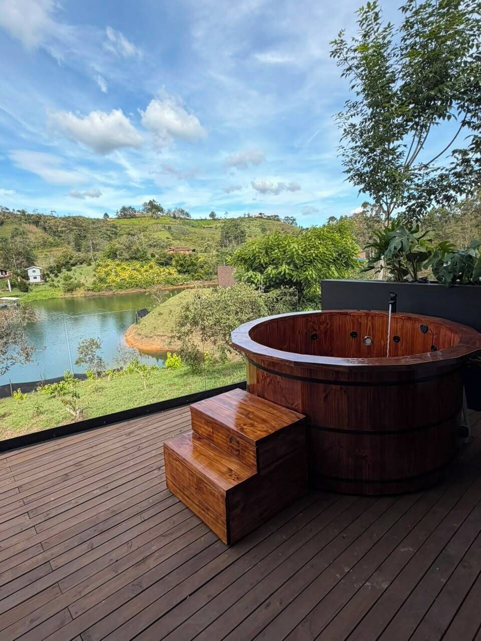 Una terraza de madera con un jacuzzi y vistas a un lago.