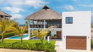 A two-story resort with a pool, thatched-roof structures, and a white building with a garage.