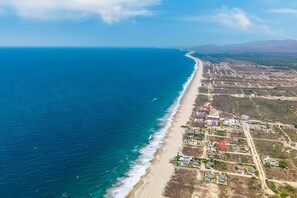 An aerial view of a coastal area with a beach, residential buildings, and a clear sky.