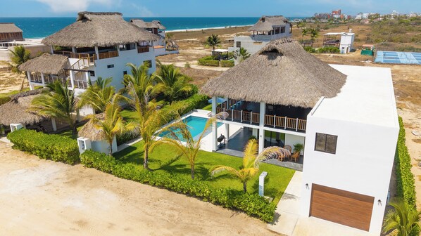 A beachfront property with multiple buildings, a swimming pool, and thatched-roof structures.