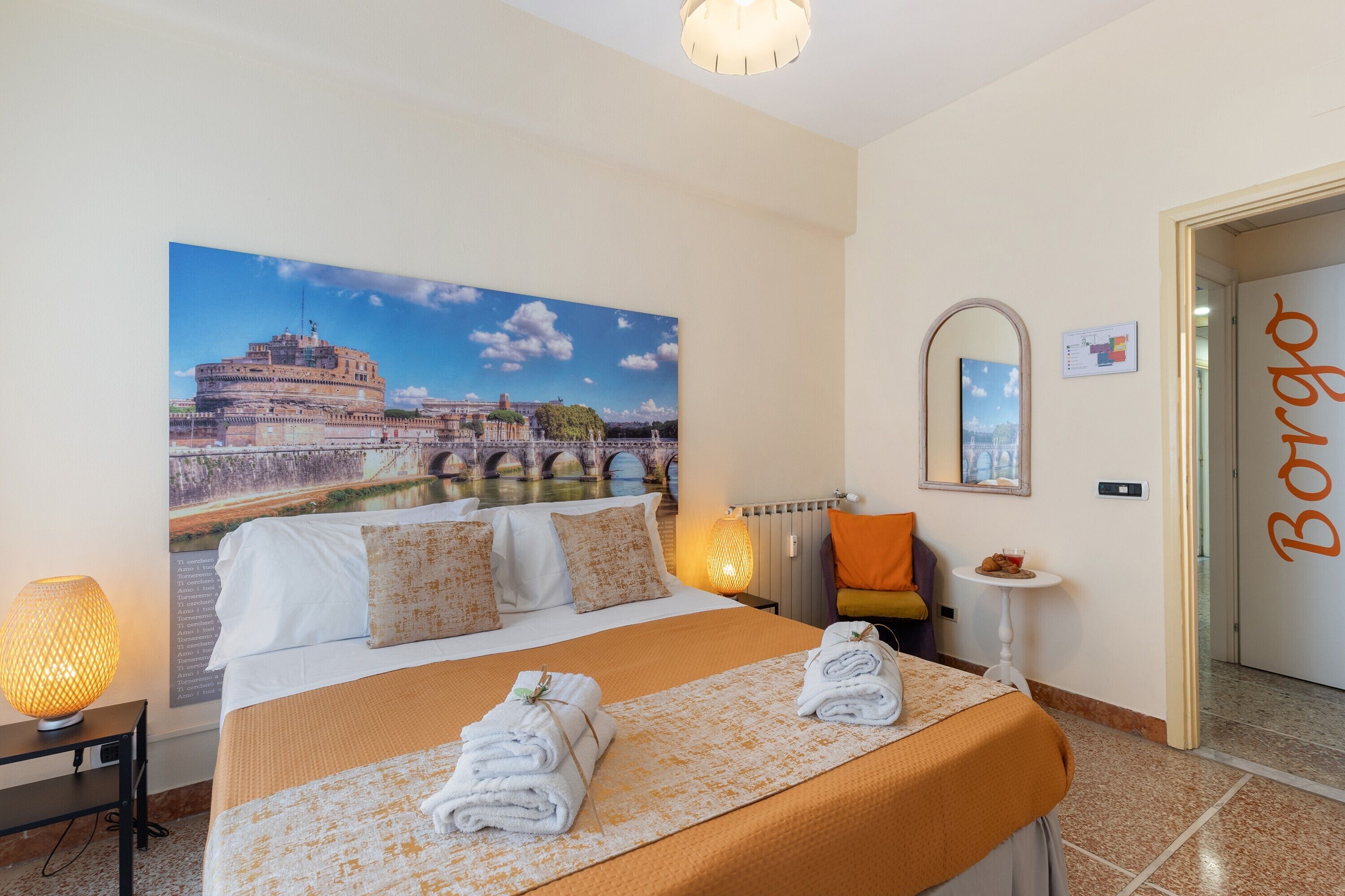 Une chambre d’hôtel avec un grand lit, une vue sur un bâtiment historique, un miroir, une petite table avec une boisson et une porte portant l’inscription « Borgo ».