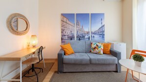 En moderne stue med sofa, skrivebord, stol, lampe og et spejl på væggen.