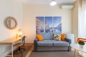 A modern living room with a sofa, a desk, a chair, a lamp, and a wall-mounted mirror. - Room 'Camera Familiare - Borgo' with Balcony, Wi-Fi and Air Conditioning (Rome)