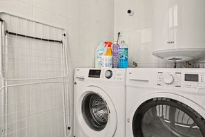 A laundry area with a front-loading washer and dryer, a metal drying rack, and a sink with a faucet.