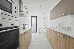 A modern kitchen with built-in appliances, a dining area, and a view through an open door.