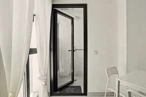 Une pièce avec une porte donnant sur une salle de bain, une chaise blanche et un paillasson sur lequel est écrit « Bienvenue à la maison ».