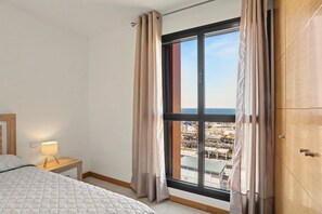 Een slaapkamer met een bed, een bedlamp, een raam met gordijnen en uitzicht op de stad.
