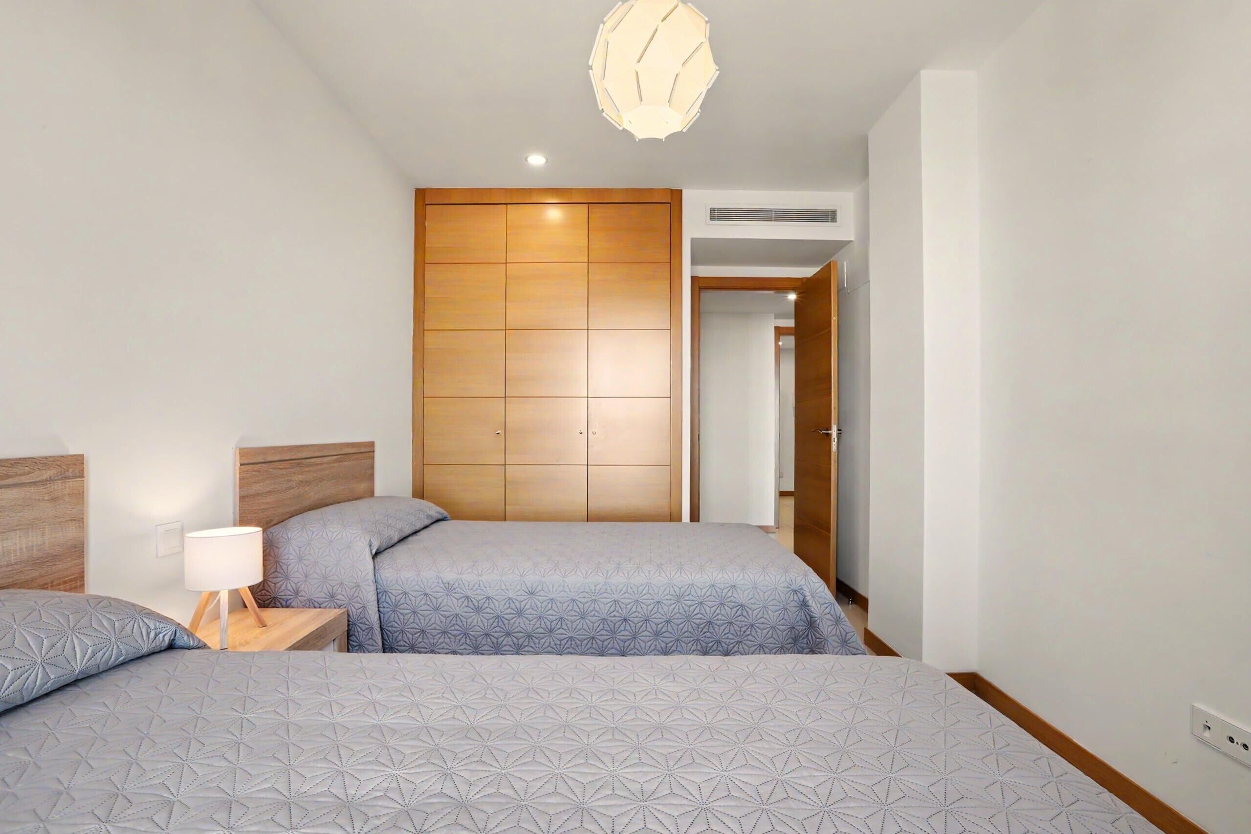 Une chambre avec deux lits, une armoire en bois, une table de chevet avec une lampe et un luminaire au plafond.