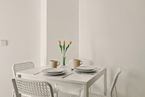 A white dining table with two chairs, a vase with yellow flowers, and two beige cups.