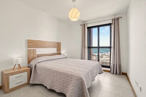 Une chambre à coucher avec un lit, une table de chevet, une lampe et une vue sur la ville grâce à une grande fenêtre.