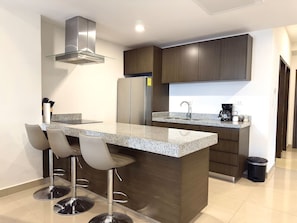 A modern kitchen with a central island, bar stools, a stainless steel range hood, and dark wooden cabinets. - Moderno Departamento en Torre 5 by GPS (Mazatlán)