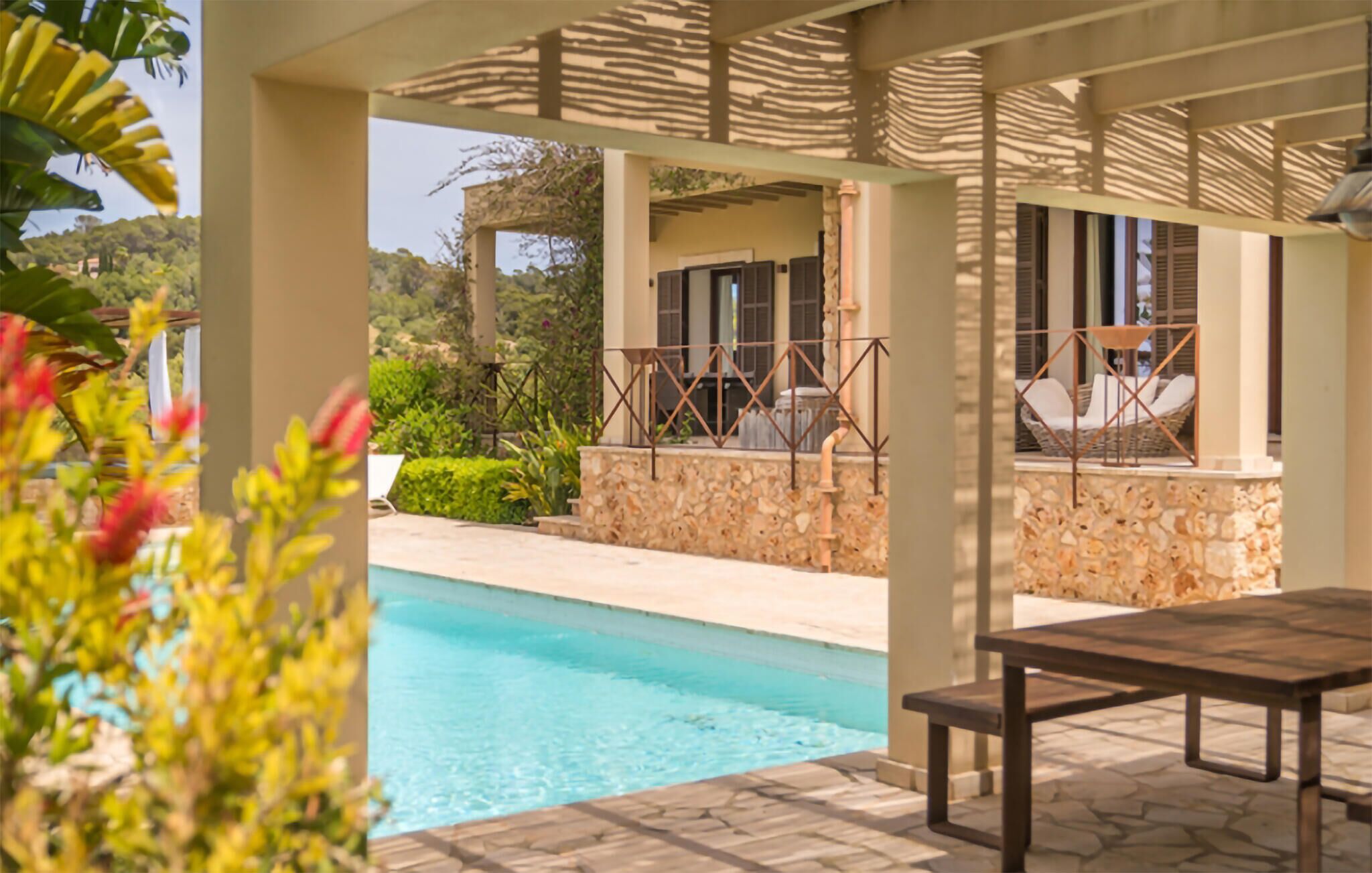 A pool area with a stone wall, outdoor seating, and a covered patio.