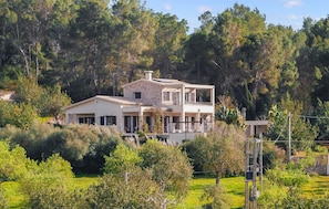 Ein zweistöckiges Haus mit Balkon, umgeben von Bäumen und Grün.