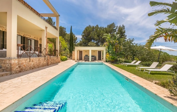 Ein Pool mit einer Steinterrasse, Liegestühlen und einem überdachten Sitzbereich.