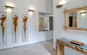 Un couloir agrémenté d’œuvres d’art abstraites sur les murs, d’un miroir et d’une console dont le plateau est en verre.