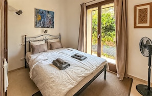 Ein Schlafzimmer mit Bett, einem Gemälde, einem Fenster mit Vorhängen und einem Ventilator.