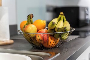 A metal fruit basket on a kitchen counter with a sink and a microwave in the background.