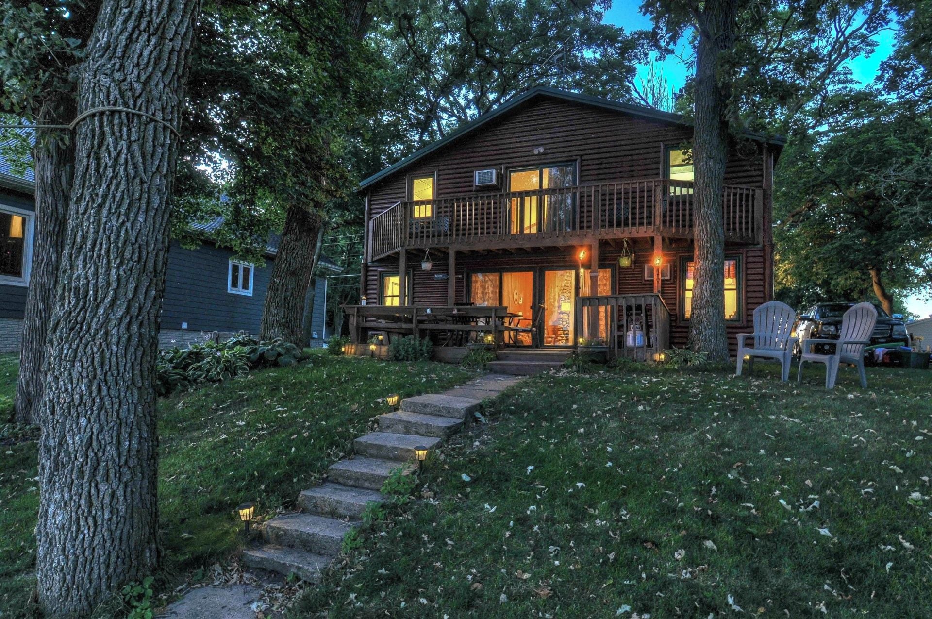 A two-story log cabin with a porch, outdoor seating, and a stone staircase leading to the entrance.