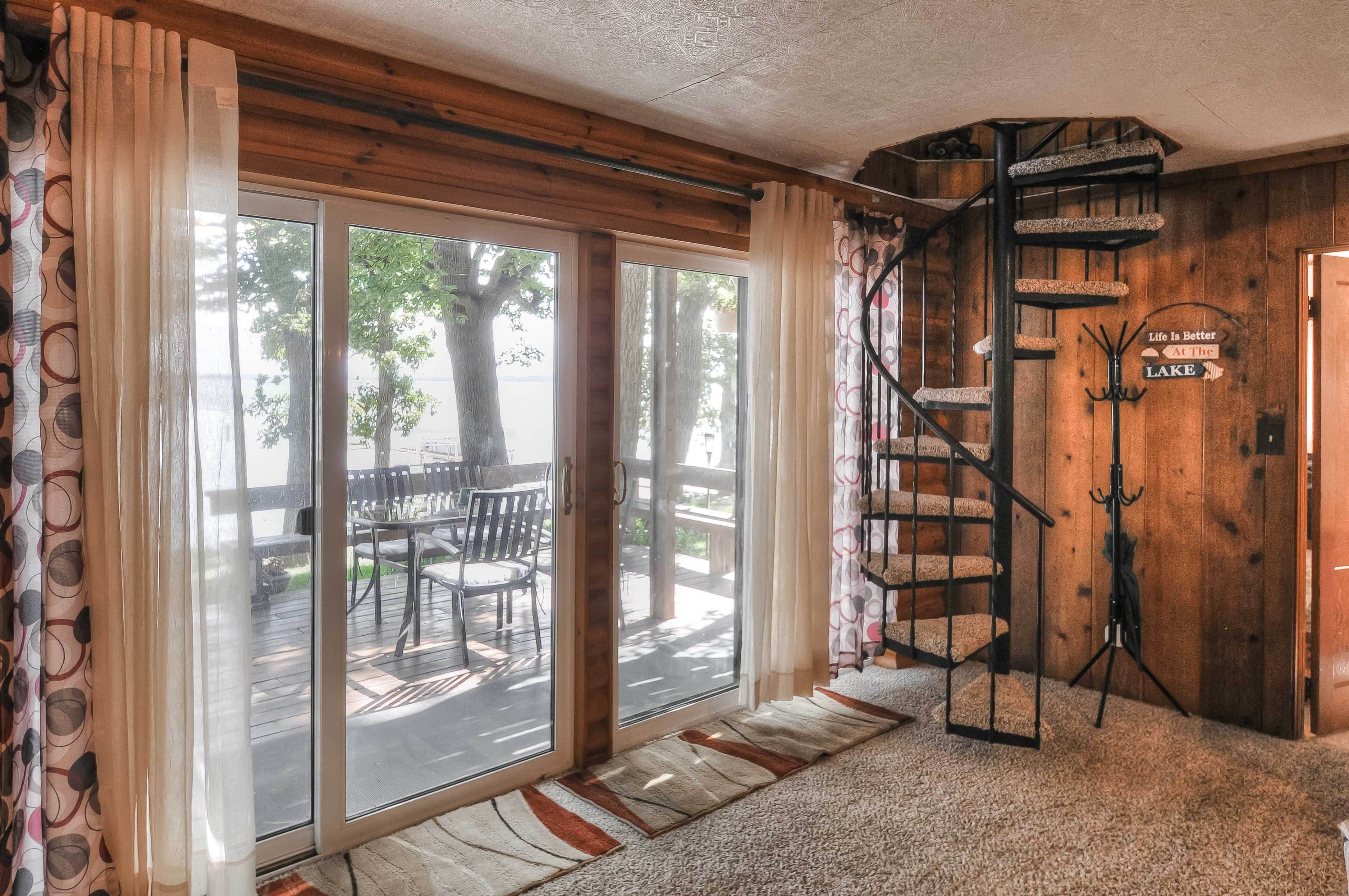 A room with a spiral staircase, a sliding glass door leading to an outdoor deck, and a sign that reads 'Life is Better At The Lake'.