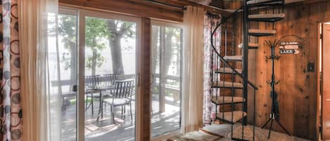 Una habitación con una escalera de caracol, un cerramiento de vidrio corredero que da a una terraza exterior, y un cartel que dice 'Life is Better At The Lake'.