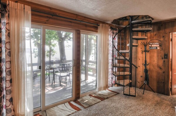 Una habitación con una escalera de caracol, un cerramiento de vidrio corredero que da a una terraza exterior, y un cartel que dice 'Life is Better At The Lake'.