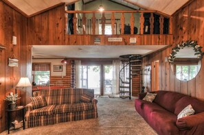 A cabin interior with a sofa, a red couch, a staircase, and a view of a lake.