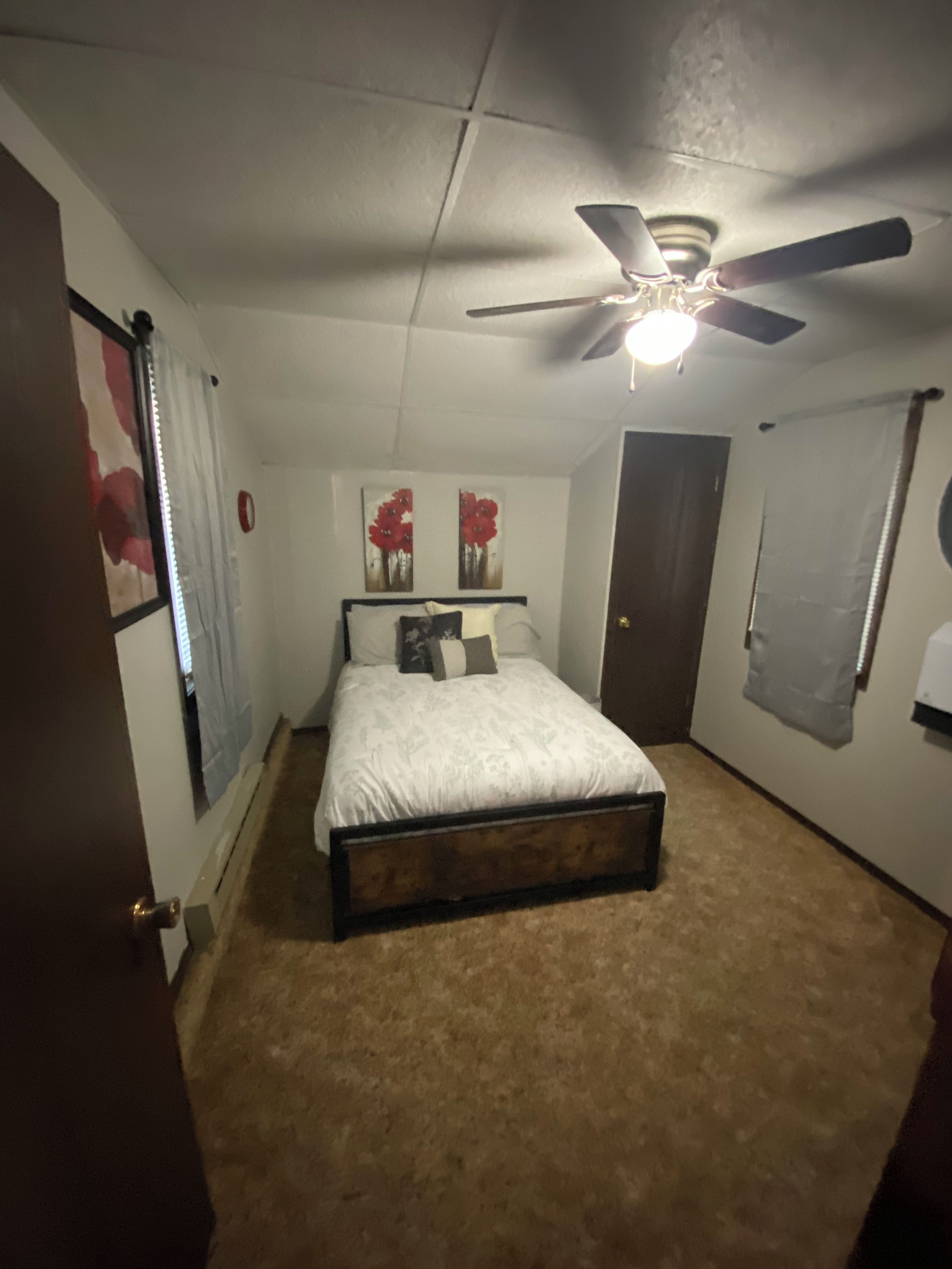 Un dormitorio con una cama, ventilador de techo y obras de arte en las paredes.