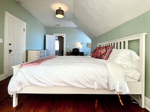 Ein Schlafzimmer mit einem weißen Bett, einer Tür, einem Schminktisch und einer Lampe.