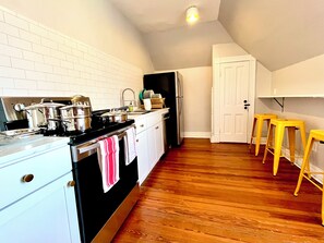 A kitchen with white cabinets, a black stove, and wooden flooring. - Caldwell's Attic — Cozy King Bed Attic Getaway + Central Location (Staunton)