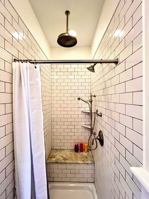Et lille bruseværelse med fliser, brusehoved, bruseforhæng og en hylde med toiletartikler.