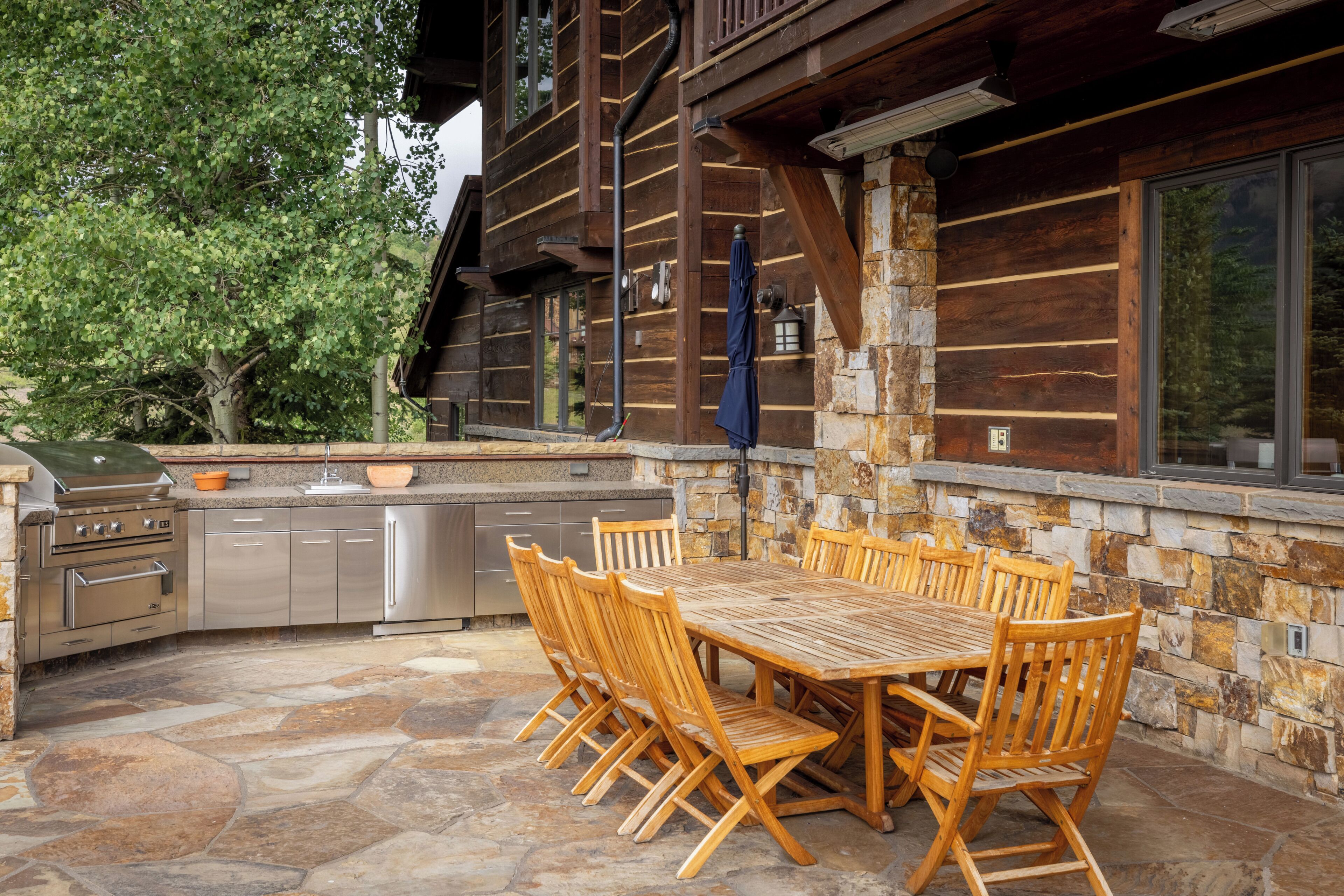 A wooden cabin with a stone exterior, a large dining table with chairs, and a built-in kitchen with stainless steel appliances.