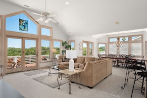 A spacious living room with large windows, a ceiling fan, and a dining area with chairs and a table. - Mermaids Pearl: Sound Views, Village Beach Club and YMCA Access, Hot Tub (Nags Head)