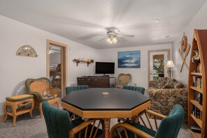A dining area with a round table, chairs, a ceiling fan, a television, and a bookshelf. - Mermaids Pearl: Sound Views, Village Beach Club and YMCA Access, Hot Tub (Nags Head)