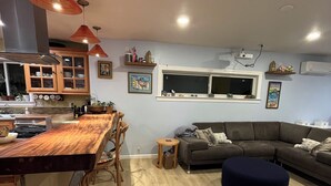 Une cuisine moderne avec un coin bar, un canapé gris et un pouf rond.