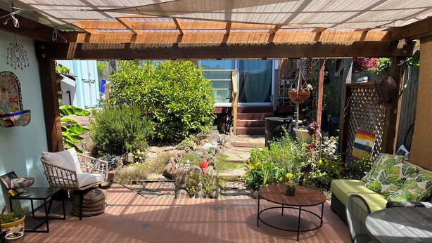 Une terrasse extérieure agrémentée d’une pergola en bois, de coins salon et de plantes en pot.