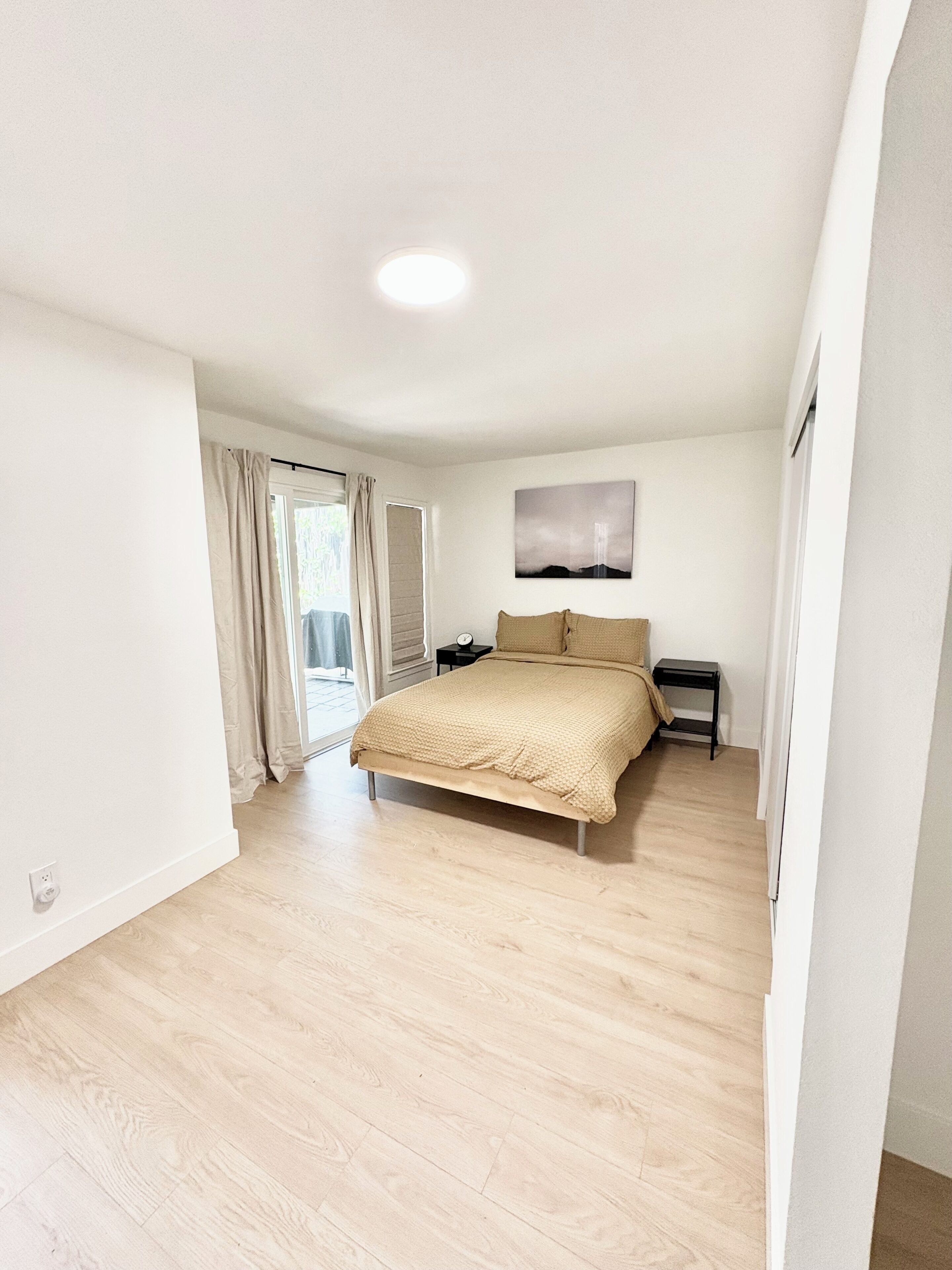 A bedroom with a bed, a nightstand, a wall-mounted lamp, and a window with curtains.