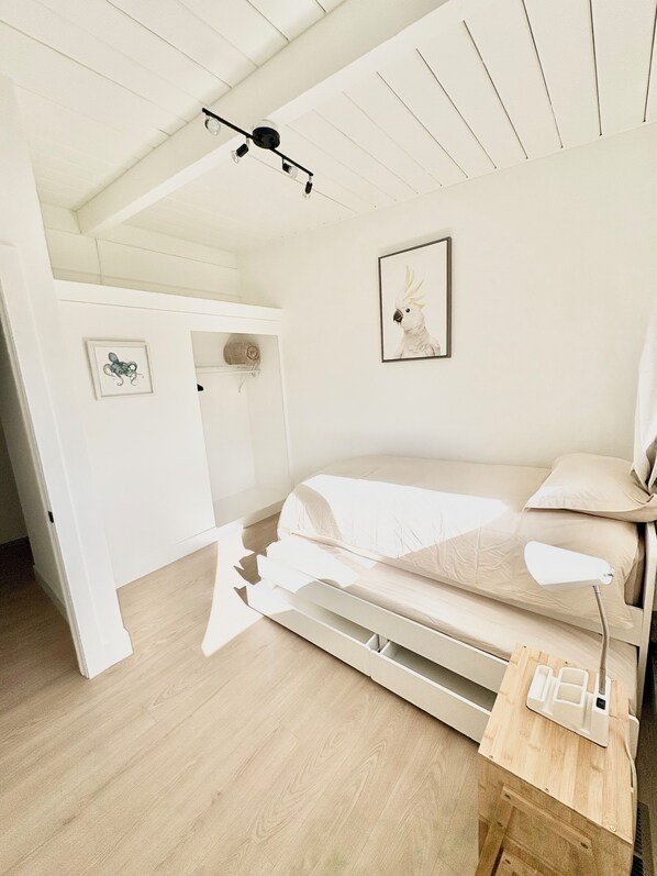A minimalist bedroom with a bed, a bedside table, a lamp, a ceiling light fixture, and a framed picture on the wall.
