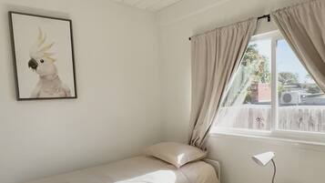 Quarto minimalista com cama, abajur, uma pequena mesa de cabeceira de madeira e uma janela com cortinas.