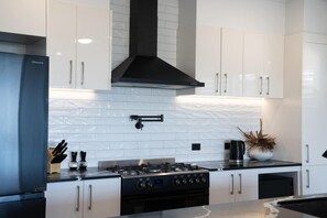 A modern kitchen with white cabinets, a black range hood, and a gas stove. - Quampi – Unbelievable Main Beach Views (Point Lookout)