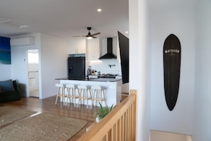 A modern kitchen with a central island, bar stools, and a ceiling fan. - Quampi – Unbelievable Main Beach Views (Point Lookout)