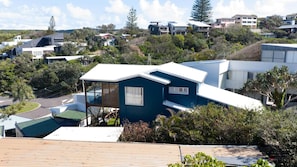 A residential area with modern houses, a prominent blue house with a balcony, and a hilly landscape. - Quampi – Unbelievable Main Beach Views (Point Lookout)