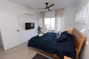 A bedroom with a bed, a ceiling fan, a TV, a window with curtains, and a door. - Quampi – Unbelievable Main Beach Views (Point Lookout)