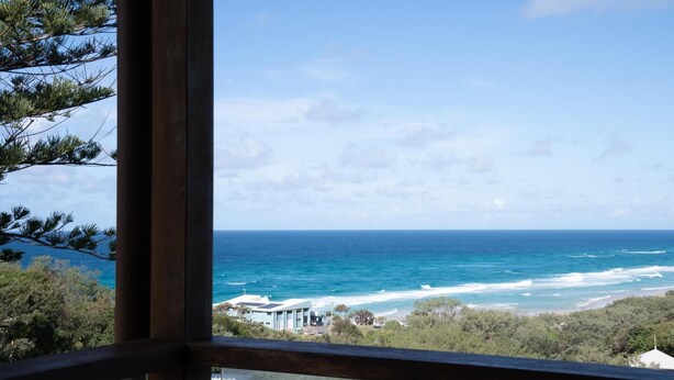 Vista sul litorale attraverso una finestra, con spiaggia, oceano e un edificio dal design moderno.