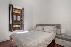 Ein Schlafzimmer mit einem Bett, einem Nachttisch, einer Lampe und einem Fenster mit Vorhängen.