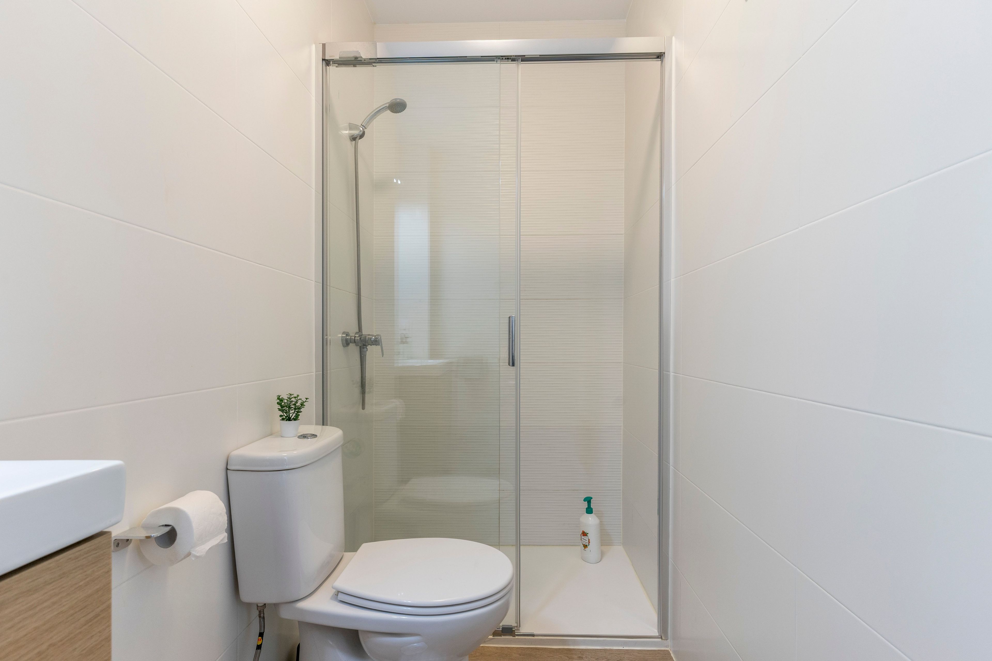 Un baño con inodoro, cabina de ducha y una pequeña estantería con una botella.