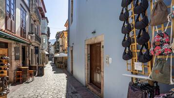Une ruelle étroite pavée de pierres, bordée de bâtiments des deux côtés, avec une porte en bois et un présentoir à sacs.